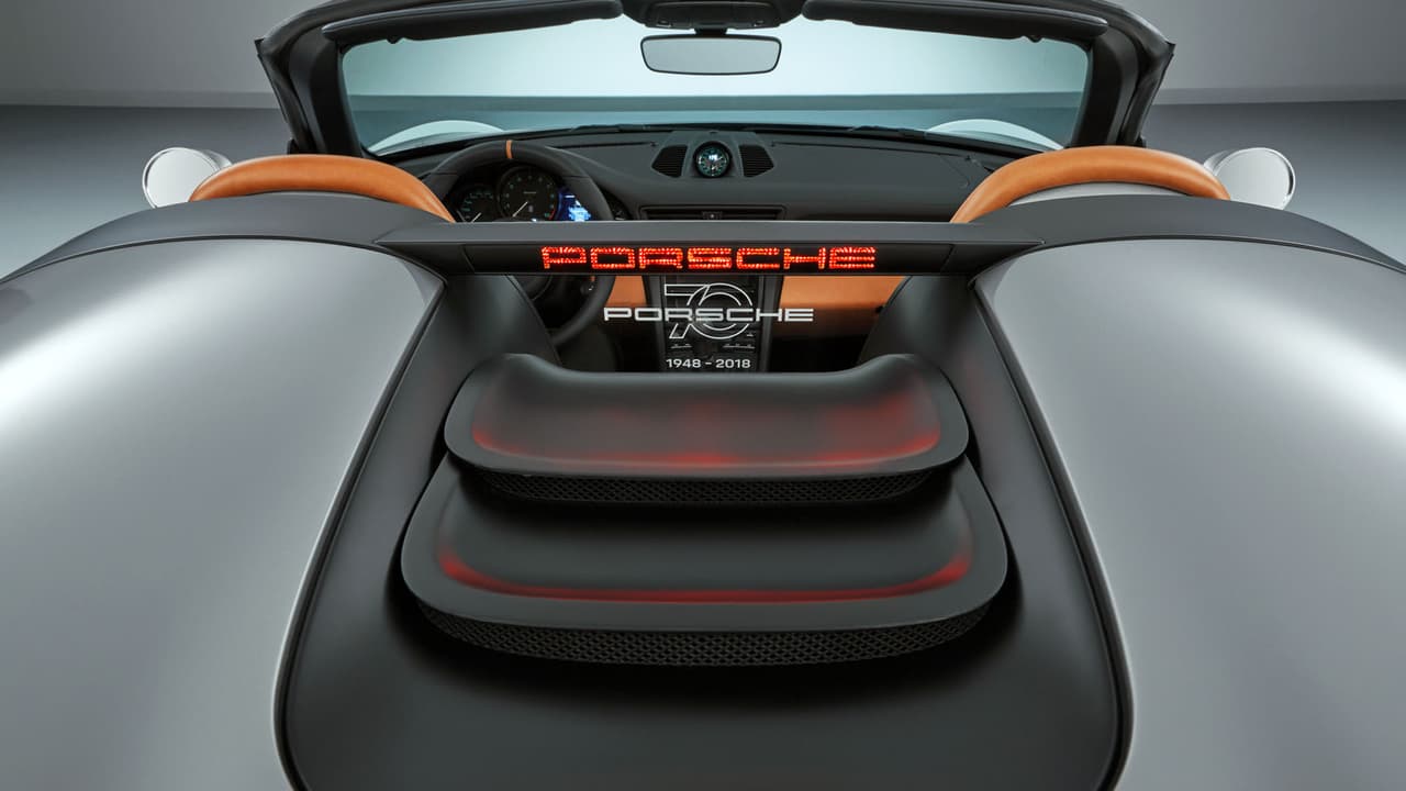 La plataforma de fibra de carbono detrás de los asientos escondiendo una barra anti-vuelcos y el pequeño cortavientos posterior plástico porta un sticker que dice “70 Years of Porsche”.