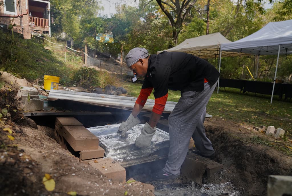 El chef Duane Tucker asa alimentos en un hoyo excavado en el suelo durante la tercera reunión anual "Finding Home" (Encontrar un hogar) de Baltimore Gift Economy, celebrada en el barrio de Collins Avenue, en Baltimore, el domingo 19 de octubre de 2025.
