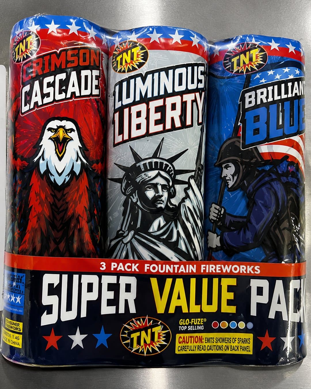 Paquete de tres fuentes de fuegos artificiales marca TNT con temática patriótica. Los cilindros muestran un águila roja, la Estatua de la Libertad plateada y un soldado azul. "Super Value Pack".