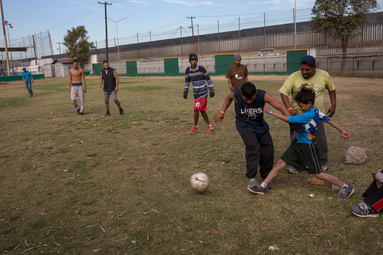 Un grupo de migrantes centroamericanos pasó el tiempo jugando fútbol en un refugio. Al fondo la valla fronteriza que separa a México de EEUU.