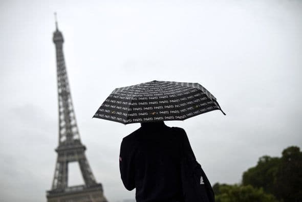 Un turista mira hacia la Torre Eiffel cubriéndose con un paraguas de la lluvia.