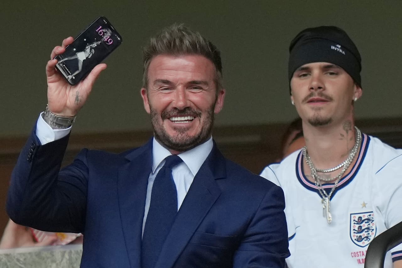 El exfutbolista inglés y presidente del Inter Miami, David Beckham, sostiene un teléfono móvil con una foto de su esposa Victoria, mientras su hijo Romeo Beckham, a la derecha, observa antes del partido de cuartos de final del Mundial entre Noruega e Inglaterra en Miami Gardens, Florida, el sábado 11 de julio de 2026.