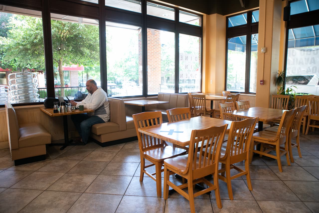 Duke Scott trabaja de forma remota en el comedor vacío del restaurante J. Christopher's el 27 de abril de 2020 en Brookhaven, Georgia. Las tablas están marcadas con una "X" para que los clientes no las usen para adherirse a los protocolos de distanciamiento social.