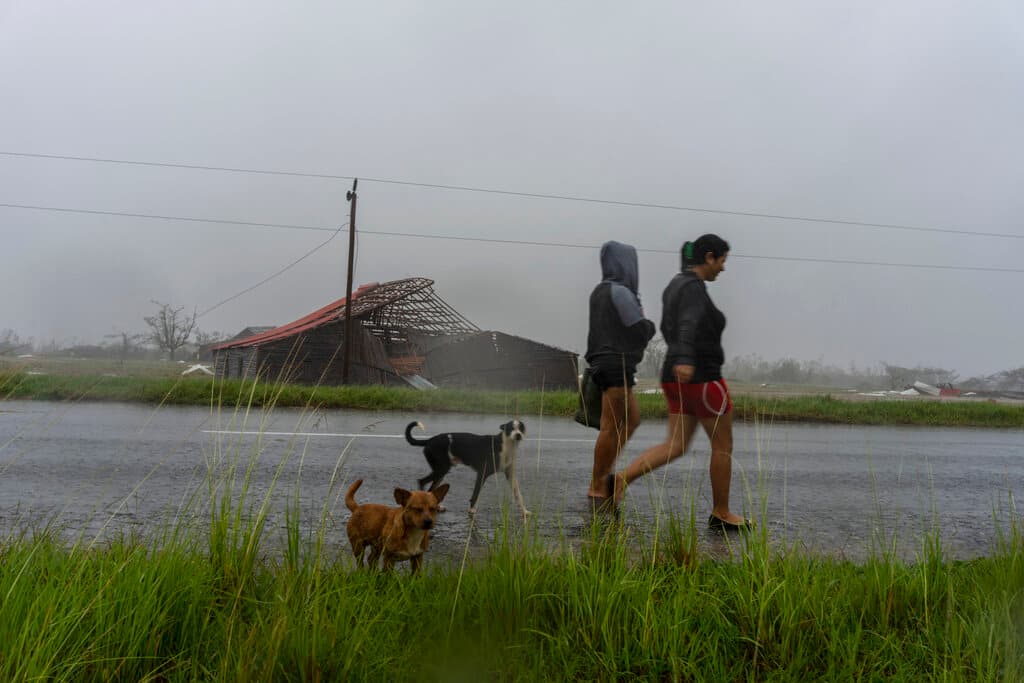 La gente camina bajo la lluvia más allá de una granja de tabaco después de que el huracán Ian golpeó en Pinar del Río, Cuba, el martes 27 de septiembre de 2022. Ian tocó tierra a las 4:30 a.m. EDT del martes en la provincia cubana de Pinar del Río.