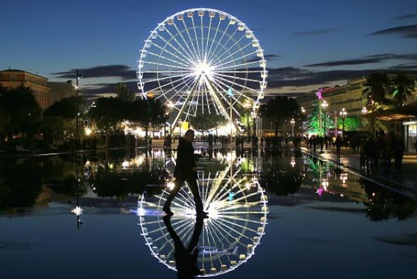Un hombre camina delante de la rueda de la fortuna en el centro de Niza, Francia.
