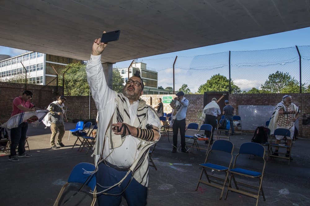 Abbi David Mason dirige el primer servicio de oración comunitaria dominical que se transmitió a su congregación desde el estacionamiento de la sinagoga Muswell Hill en Londres. La oración
<b> se llevó a cabo al aire libre con distanciamiento social para cumplir con las pautas de salud del gobierno. </b>Mason dijo que le alegraba ver a los voluntarios expertos en tecnología pasando horas en el teléfono ayudando pacientemente para que los miembros mayores de la comunidad pudieran conectarse.
<br>