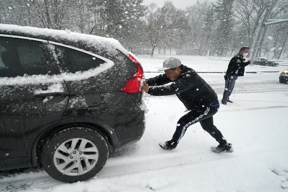 Govinda Phagami, a la izquierda, ayuda a un automovilista a subir una colina empinada en una calle totalmente cubierta de nieve en Baltimore, mientras el agente de la policía Joseph Conger, dirige desvía el tránsito durante la tormenta de nieve.