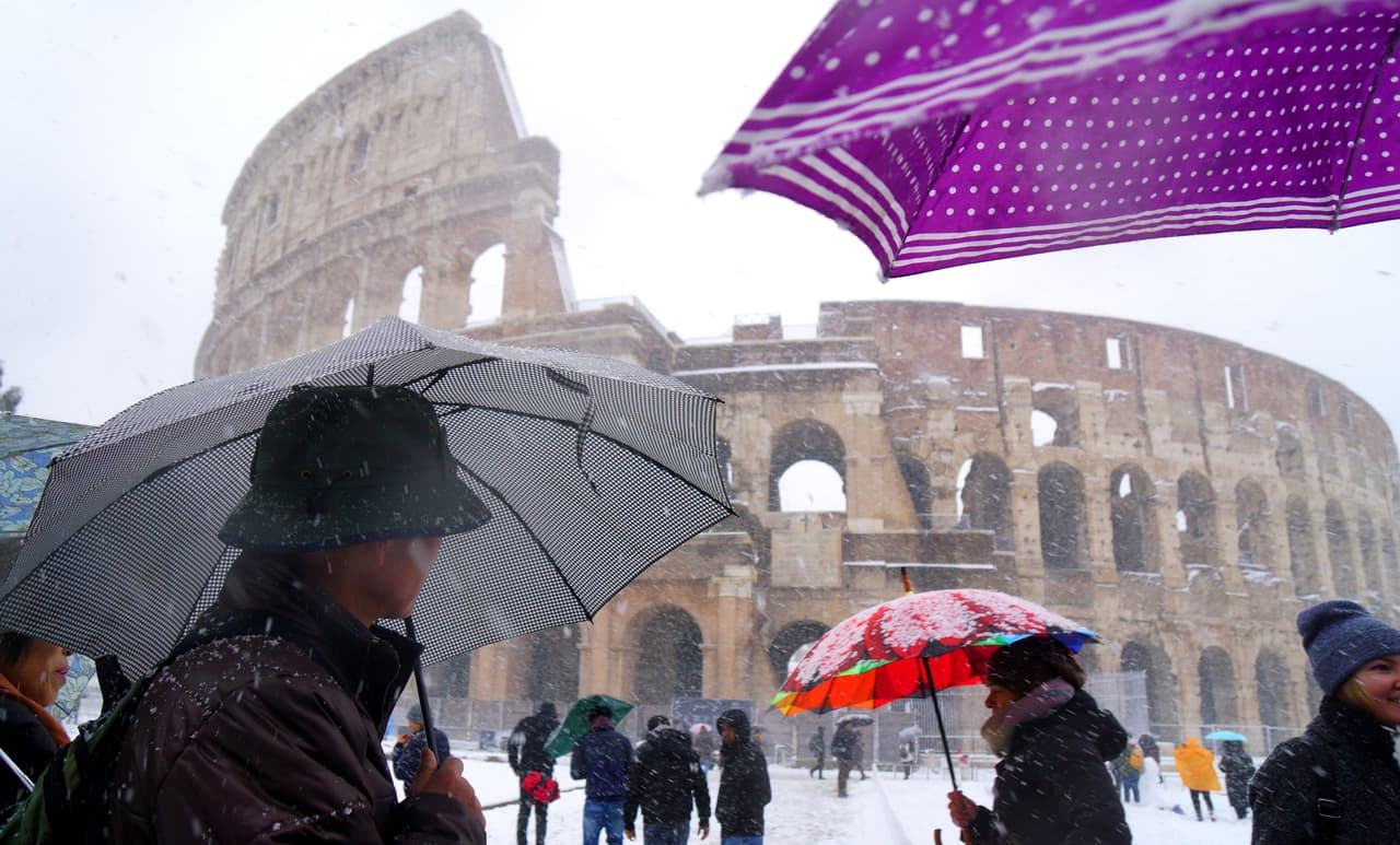 Turistas y residentes caminan frente al Coliseo de Roma bajo una intensa nevada.