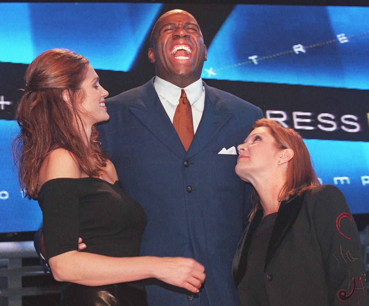 SANTA MONICA, UNITED STATES: Former US basketball player Earvin "Magic" Johnson (C) jokes with supermodel Cindy Crawford (L) and actress Carrie Fisher as they host the "Passport 99" AIDS-benefit fashion show, in Santa Monica, CA, 25 September, 1999. The annual show has raised eight million USD for HIV/AIDS research since Elizabeth Taylor created it in 1988. AFP PHOTO/Lucy NICHOLSON/ln (Photo credit should read LUCY NICHOLSON/AFP/Getty Images)