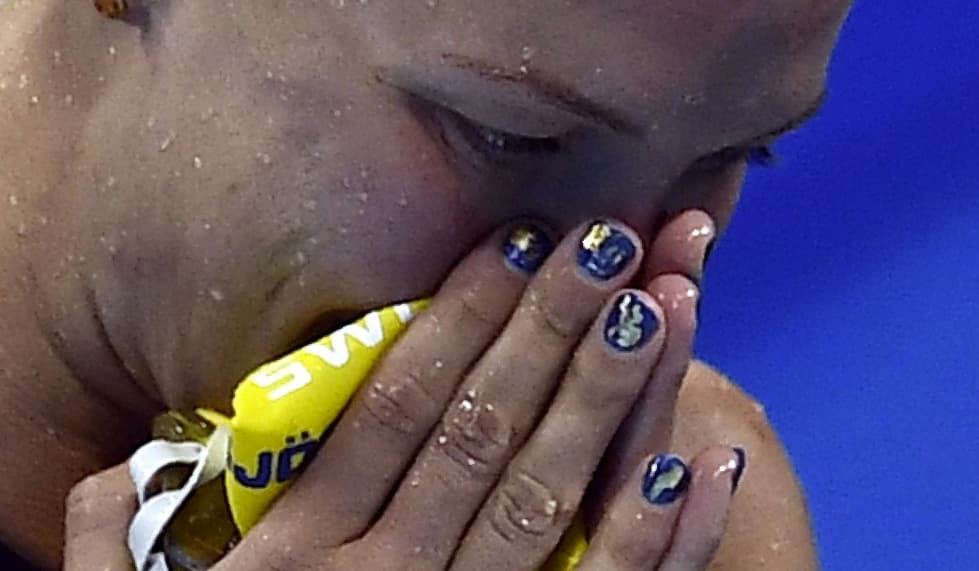 La nadadora Sueca, Sarah Sjostrom festeja su triunfo tras romper el récord mundial en 100 metros durante la final de la prueba de nado de mariposa. Parece que el decorado de sus uñas azul con toques dorados, le trajó buena suerte.