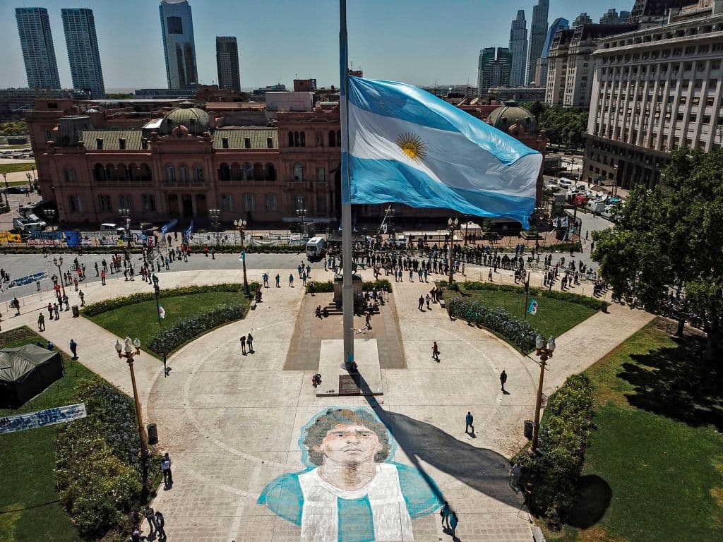 Vista aérea de la Plaza de Mayo. Al frente de la bandera argentina, la imagen trazada por aficionados de Diego Armando Maradona con la playera de la selección. La gente salió a las calles de manera masiva para asistir a la Casa Rosada donde se vela el cuerpo del astro del 
<a href="https://www.tudn.com/futbol/diego-armando-maradona-murio-a-los-60-anos-de-edad?_ga=2.214904151.1986701122.1606144710-870222659.1604003405" target="_blank">fúbol fallecido</a> el miércoles 25 de noviembre.