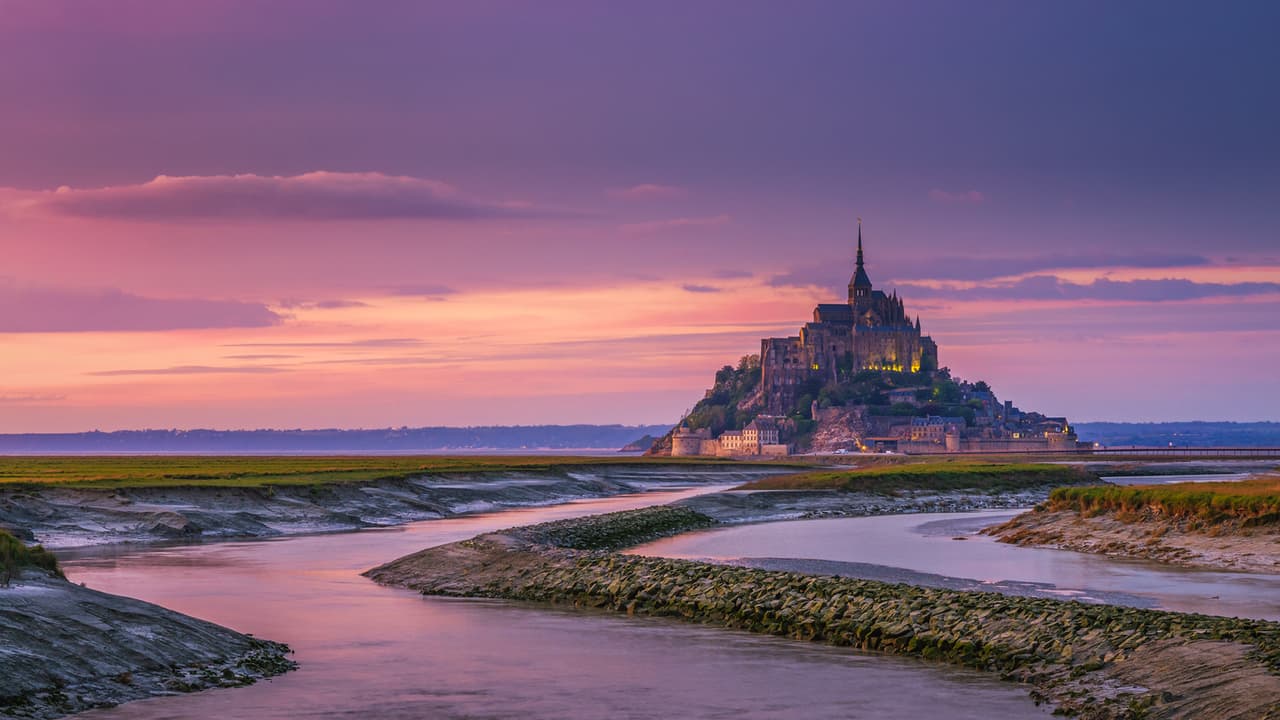 <b>Mont Saint-Michel, Francia.</b> El perfil de este pequeño islote sobresale en las costas de Normandía, ubicado en bancos de arena que surgen cuando las mareas bajan. Antiguamente, la isla solo era accesible cuando el agua se retiraba, lo que le daba una defensa natural. En la cima, se ve la aguja de una abadía benedictina gótica dedicada al arcángel San Miguel construida entre los siglos XI y XVI y rodeada de un pequeño pueblo. 
<a href="https://whc.unesco.org/en/list/80/" target="_blank">Mont Saint-Michel y su bahía son también patrimonio mundial</a> declarado por UNESCO.