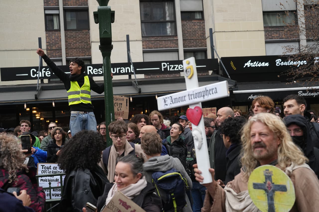 Un manifestante sostiene una cruz con la inscripción "El amor triunfará" durante una de las protestas parisinas del sábado 24 de octubre de 2026