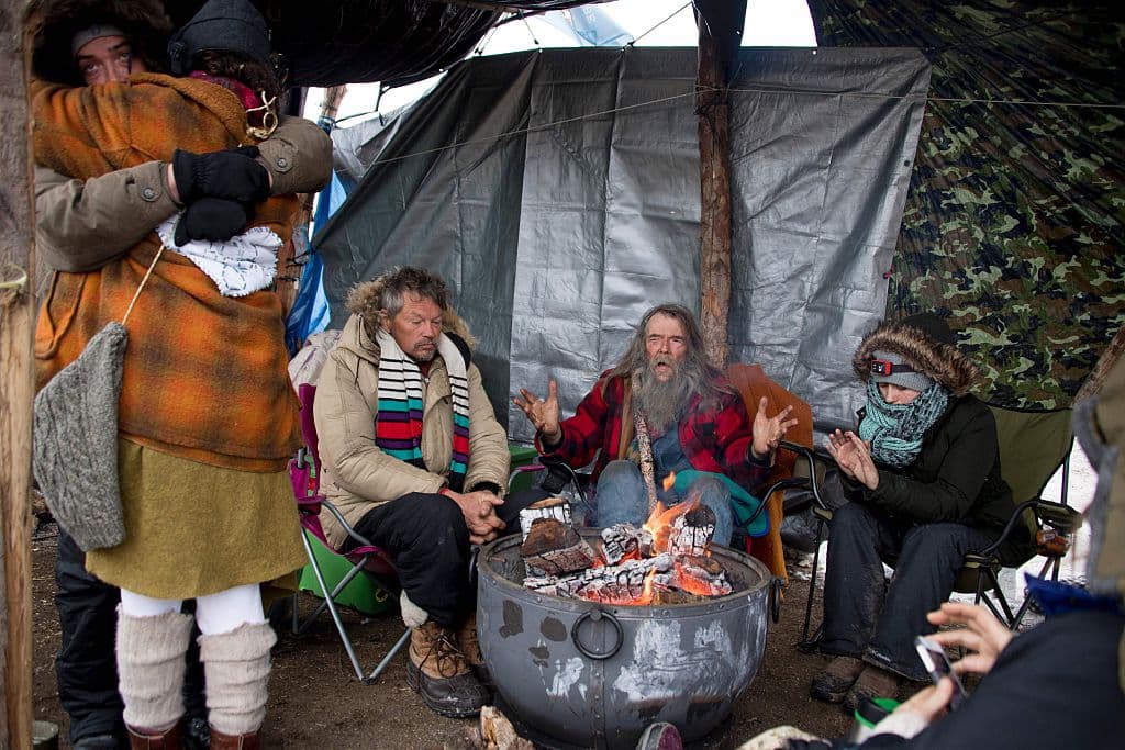 Activists hug and warm themselves by a fire at Oceti Sakowin Camp on the edge of the Standing Rock Sioux Reservation on December 5, 2016 outside Cannon Ball, North Dakota. The US Army Corps of Engineers on December 4, nixed plans for a controversial oil pipeline crossing in North Dakota, a major victory for Native Americans and environmentalists who had staged months of protests. The pipeline had been set to cross under the Missouri River and man-made Lake Oahe, which are drinking water sources for the Standing Rock Sioux Tribe. / AFP / JIM WATSON (Photo credit should read JIM WATSON/AFP/Getty Images)