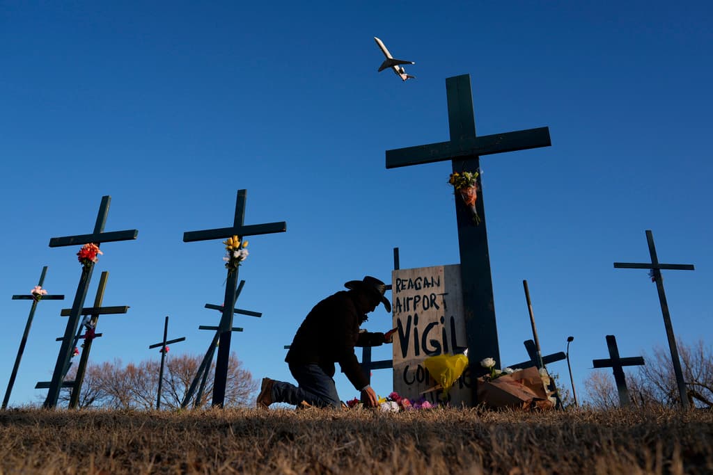 Un avión despega del Aeropuerto Nacional Ronald Reagan de Washington mientras Roberto Marquez, de Dallas, coloca flores en un memorial de cruces que erigió en honor a las 67 víctimas de la colisión aérea entre el helicóptero del Ejército y el avión de American Airlines, el sábado 1 de febrero de 2025, en Arlington, Virginia.