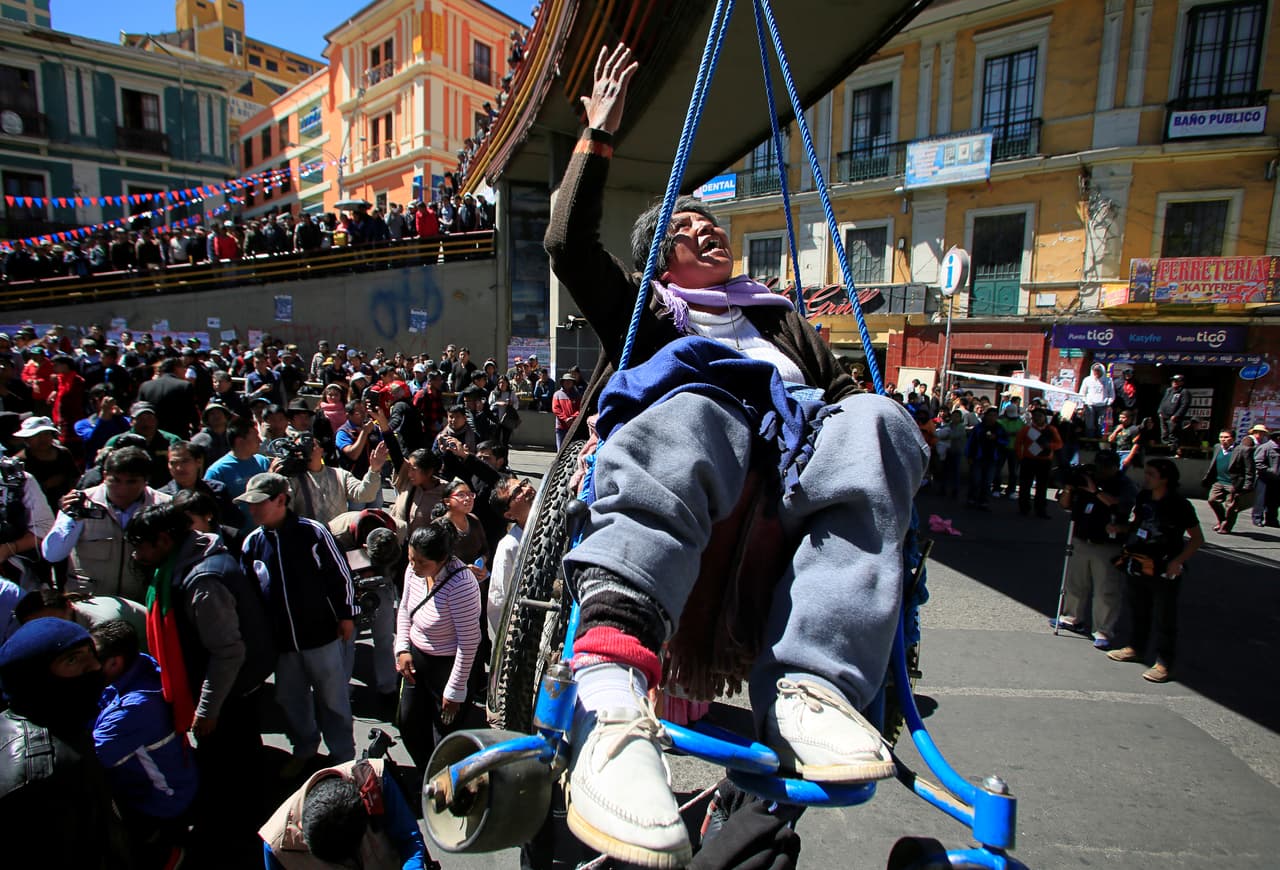 Una mujer discapacitada es levantada desde un puente peatonal, con cuerdas atadas a su silla de ruedas.