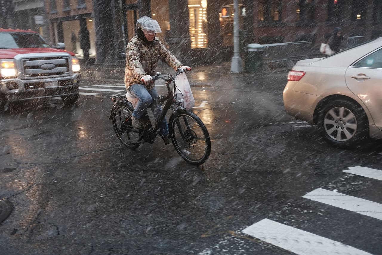 Peatones, ciclistas y autos siguen su camino a pesar de la nevada en Manhattan.