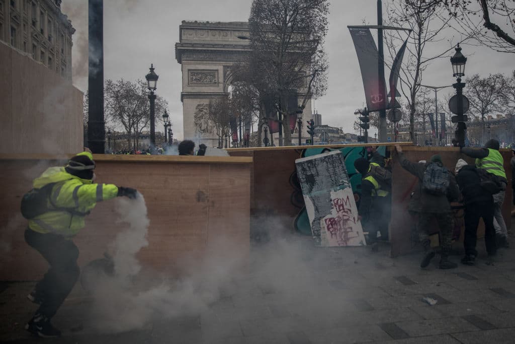 Manifestantes se esconden tras barricadas durante la protesta que registró cerca de 1,400 detenciones el sábado 8 de diciembre.
