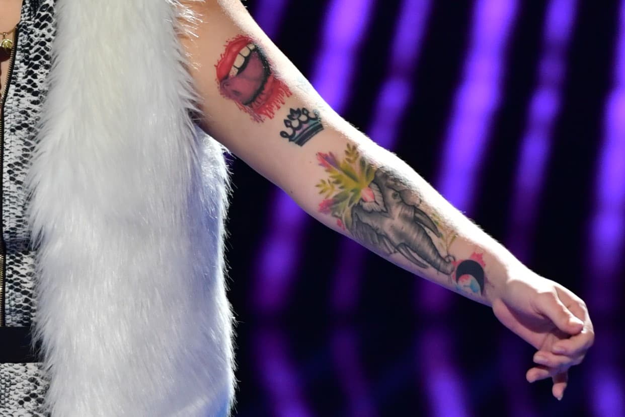 En la parte delantera del brazo izquierdo se ve una boca, una corona y un elefante.