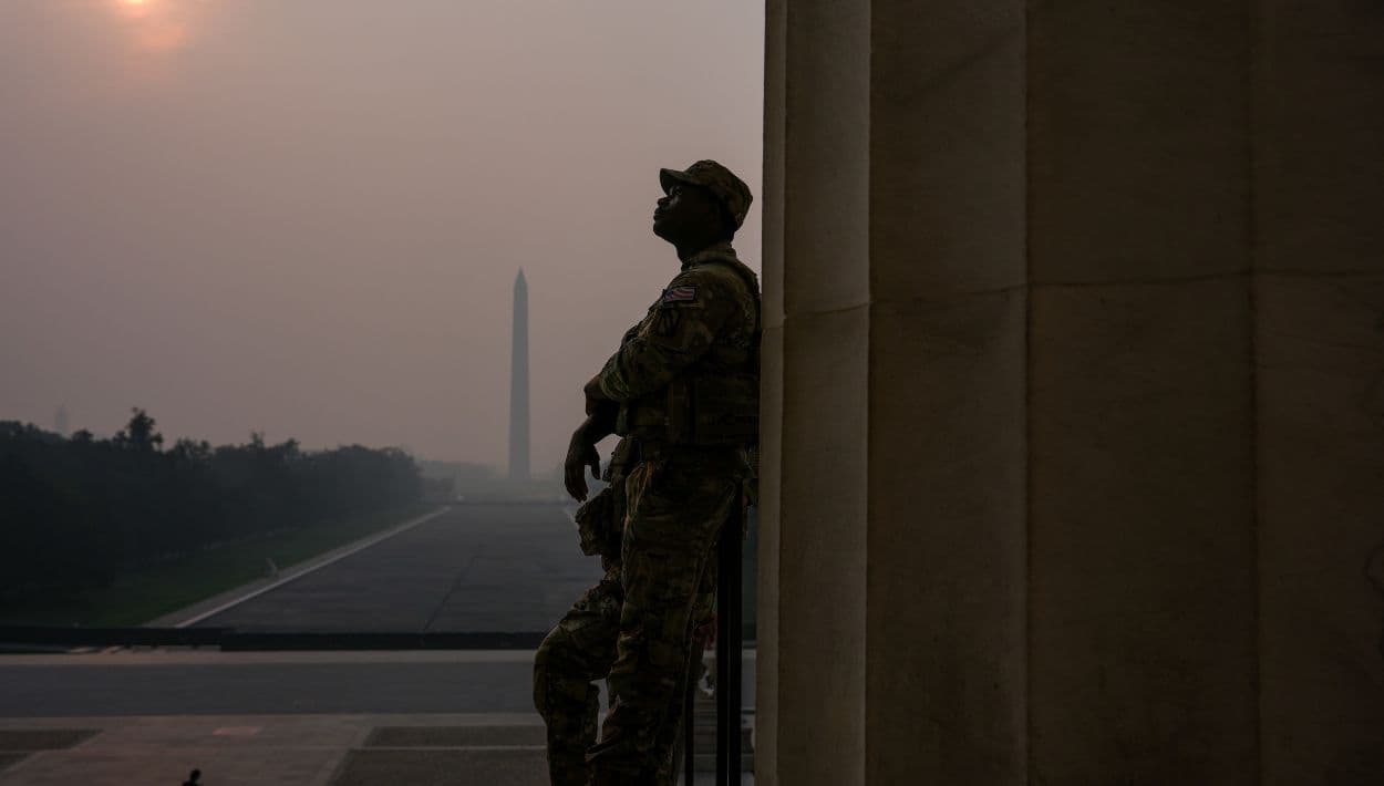 Miembros de la Guardia Nacional patrullan el Monumento a Lincoln mientras el sol, oculto por el humo de los incendios forestales, se eleva sobre el Monumento a Washington y el Reflecting Pool, el viernes 17 de julio de 2026, en el National Mall de Washington D.C.