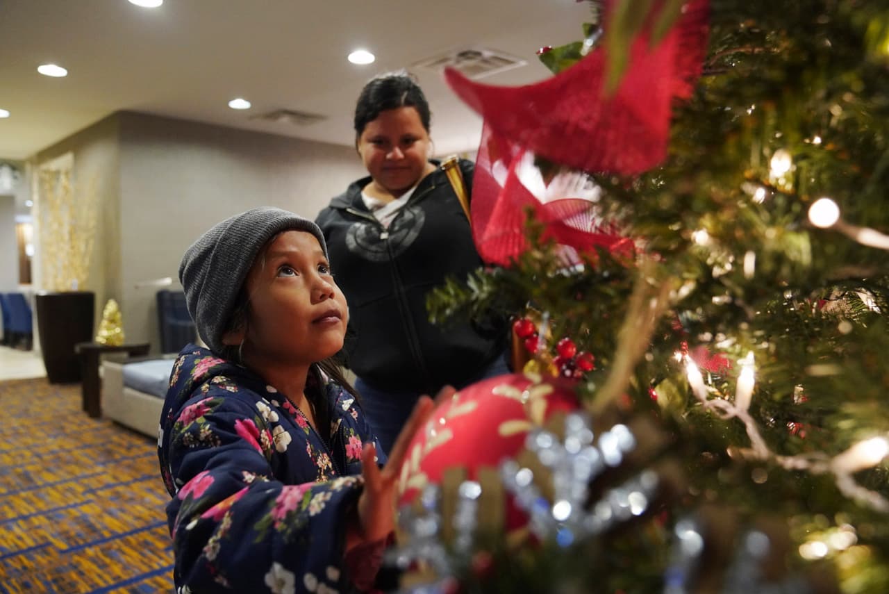 Una niña de 7 años observa un árbol de Navidad en el hotel donde ella y su madre, Isabel de 21 años, pasarán la noche tras ser procesadas en el puerto de entrada de Brownsville, Texas, el martes 17 de diciembre de 2019. (AP Foto/Veronica G. Cardenas)