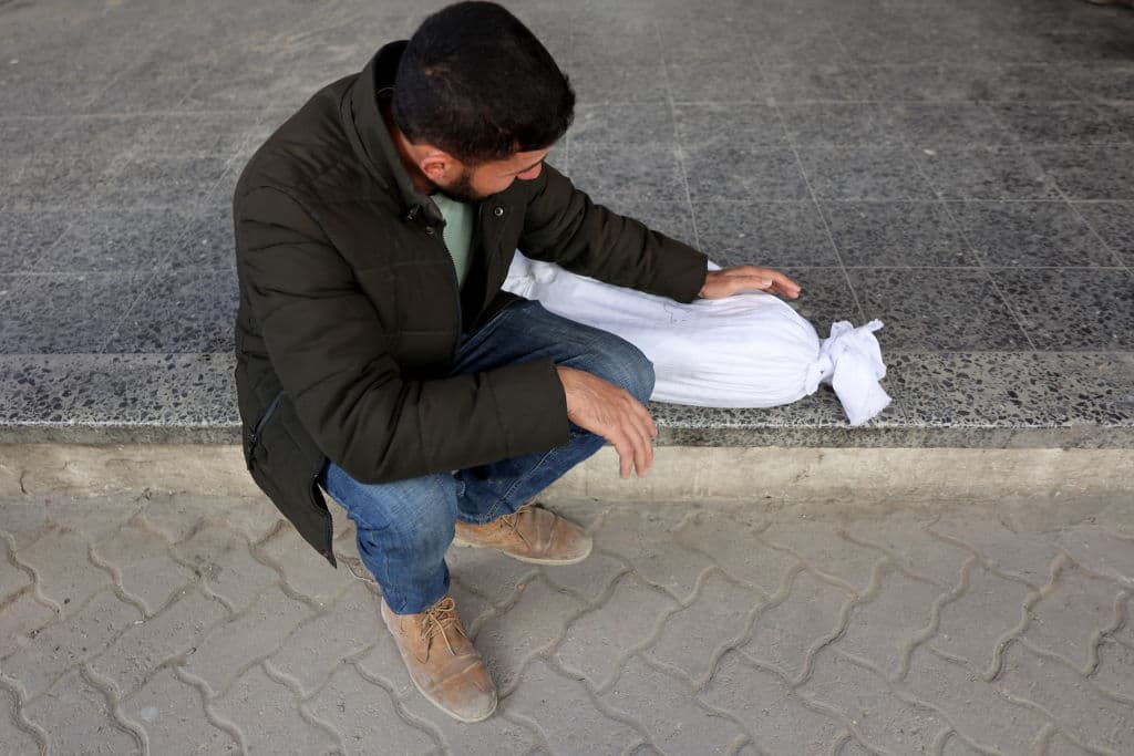 Un hombre llora el cuerpo de un niño envuelto en una tela blanca en el exterior del hospital bautista de la ciudad de Gaza, antes de un funeral el 27 de diciembre de 2024.