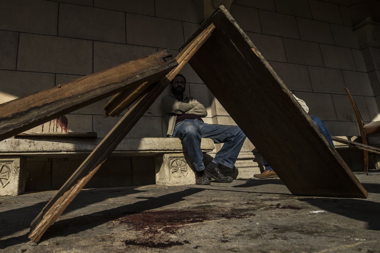 Un hombre sentado junto a una manchas de sangre en una pared en la escena de la explosión.