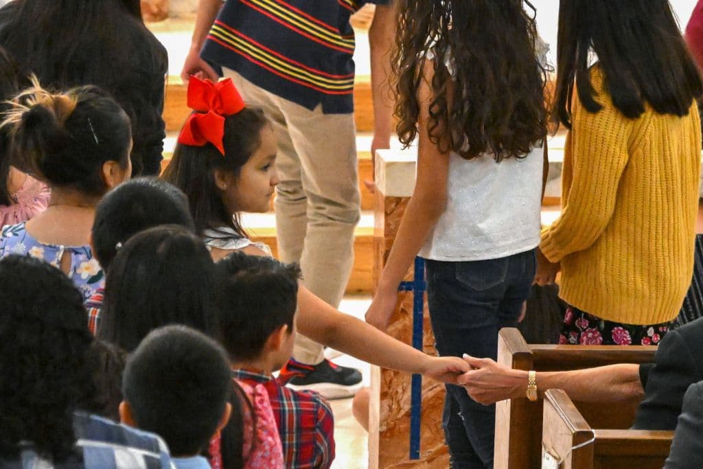 En la foto, Jill Biden toma la mano de una niña en medio de la misa. Jill Biden tocó las manos de varias personas en la misa concurrida por unas 600 personas en la Iglesia Católica del Sagrado Corazón.