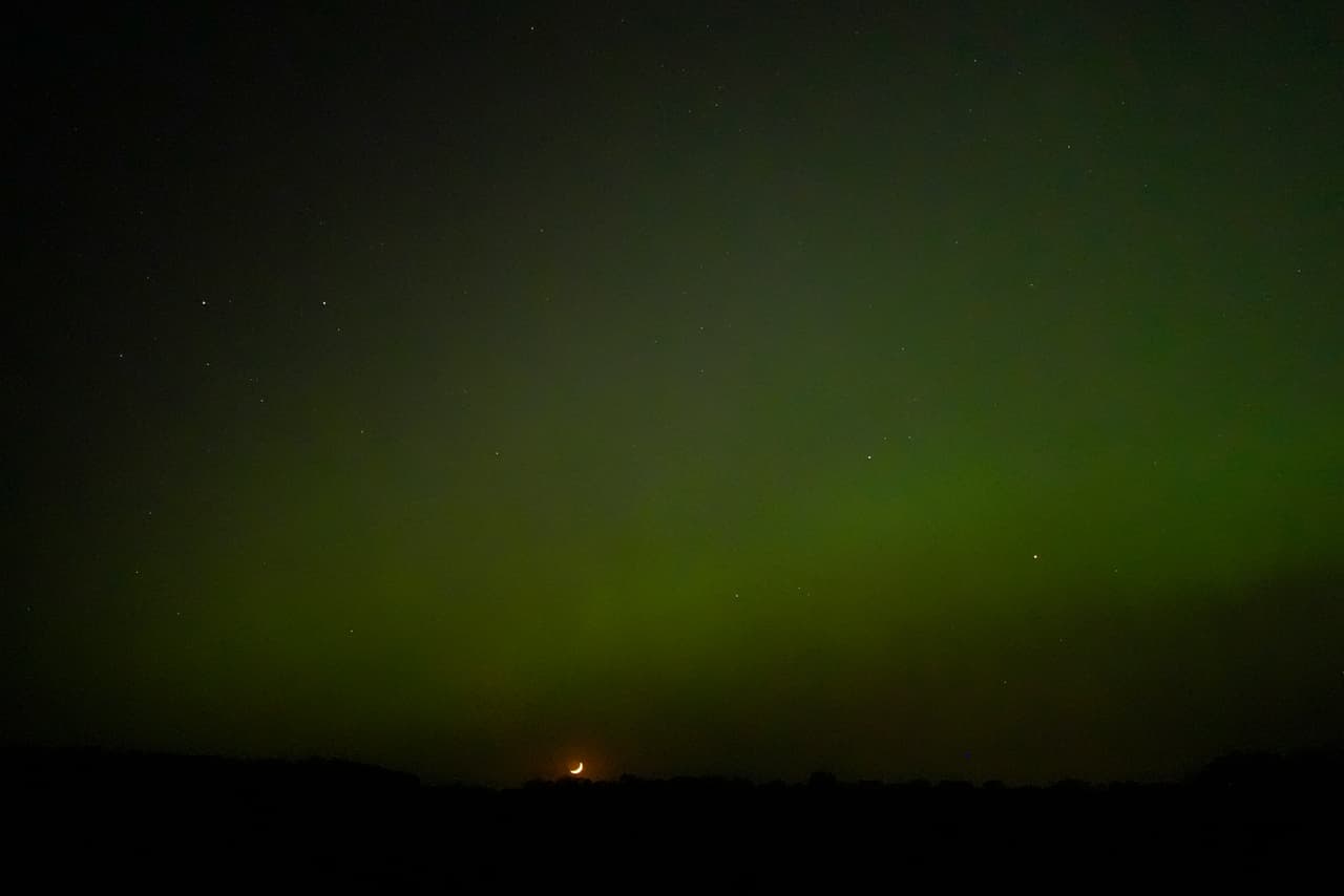 La luna creciente se pone debajo de la aurora boreal el sábado 11 de mayo de 2024, cerca de Skidmore, Missouri