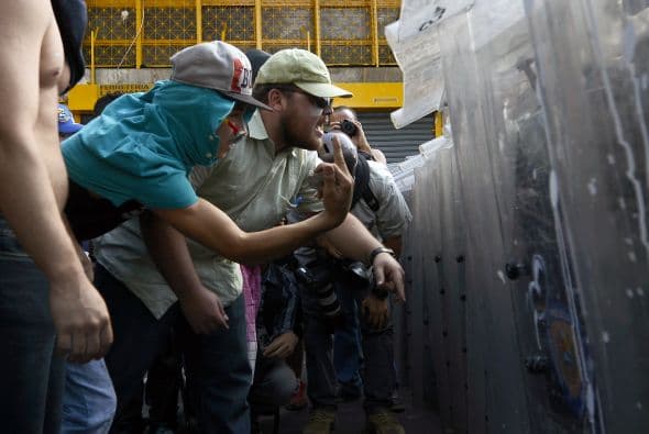 Los estudiantes, desarmados, gritan a los policías parapetados tras una cortina plástica. Los estudiantes llevaron a cabo una manifestación pacífica contra el régimen del mandatario Nicolás Maduro el 12 de febrero de 2014. Motorizados uniformados y con sus caras cubiertas, dispararon contra los manifestantes, matando a dos estudiantes y a un oficial.