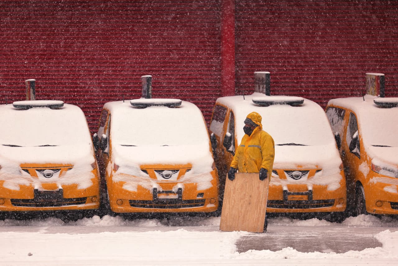 Un hombre se toma un descanso de empujar la nieve de una acera frente a los taxis amarillos cubiertos de nieve en Brooklyn