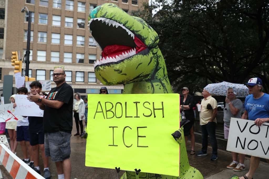 Otra botarga inflable, pero en Fort Worth sostiene esta pancarta con consignas contra ICE.