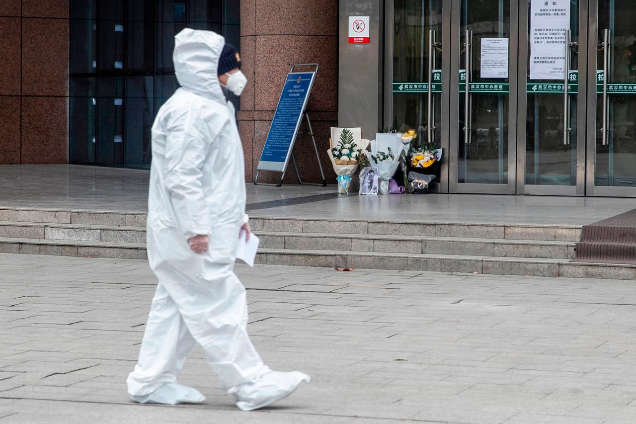 Un miembro del personal médico protegido con un traje pasa frente a un pequeño altar de flores y la fotografía de Wenliang, colocada en una entrada del Hospital Central de Wuhan. En este centro asistencial de la ciudad donde se originó el brote trabajaba el oftalmólogo, y allí fue donde falleció esta madrugada. El pasado 1 de febrero anunció que había sido contagiado del coronavirus tras haber atendido semanas antes a una mujer afectada de glaucoma.