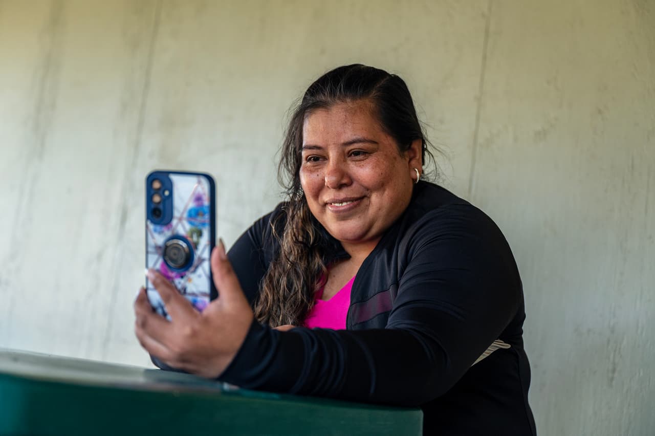 Reyna Hernández durante una videollamada por WhatsApp con algunos de sus hijos, quienes viven en Mataquescuintla, Guatemala, el martes, 18 de julio de 2023. Los hijos de Hernández estaban sentados fuera de la casa, turnándose al teléfono para ponerla al tanto de cómo estaban.