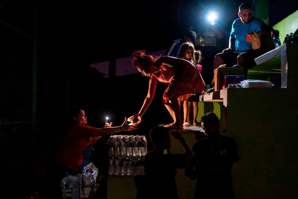 La gente comparte comida y agua en un campo de béisbol donde duermen al aire libre en Guánica, Puerto Rico, el 9 de enero de 2020, luego de que un poderoso terremoto azotara la isla.