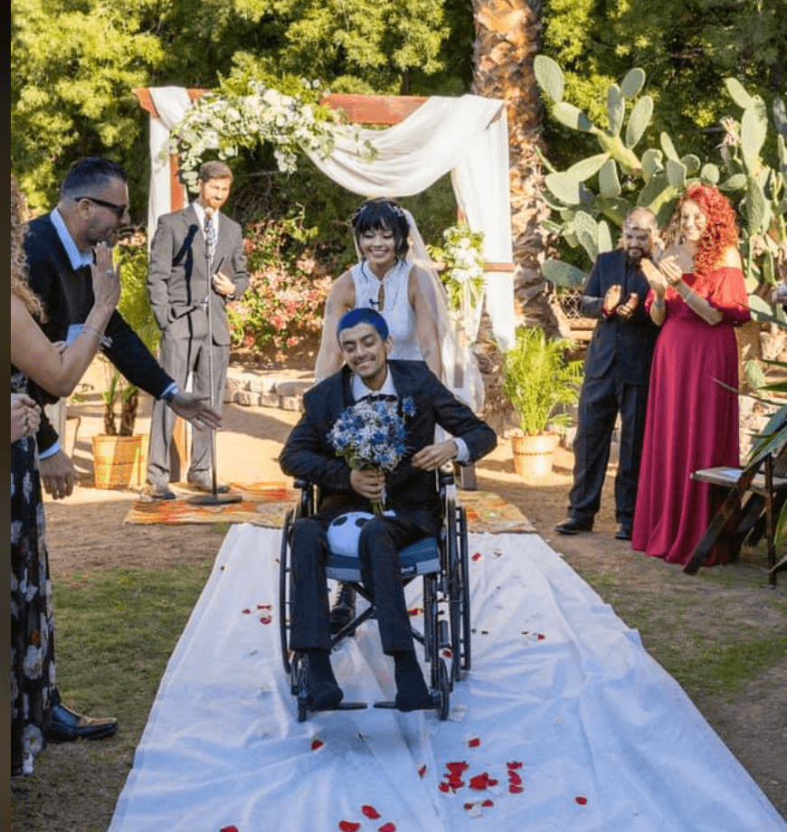 Tras la ceremonia, la novia radiante empujó la silla de ruedas de su esposo mientras él llevaba el ramo de flores armado con el color favorito de ella: azul.