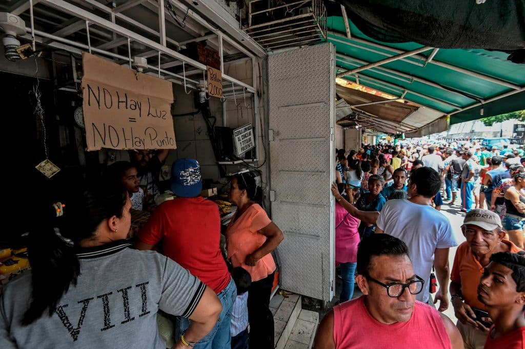Personas hacen fila para comprar comida en Petare este domingo. En un cartón se lee: No hay luz, no hay punto. En Venezuela hay escasez de efectivo y no hay punto significa que tampoco es posible pagar con una tarjeta de crédito.