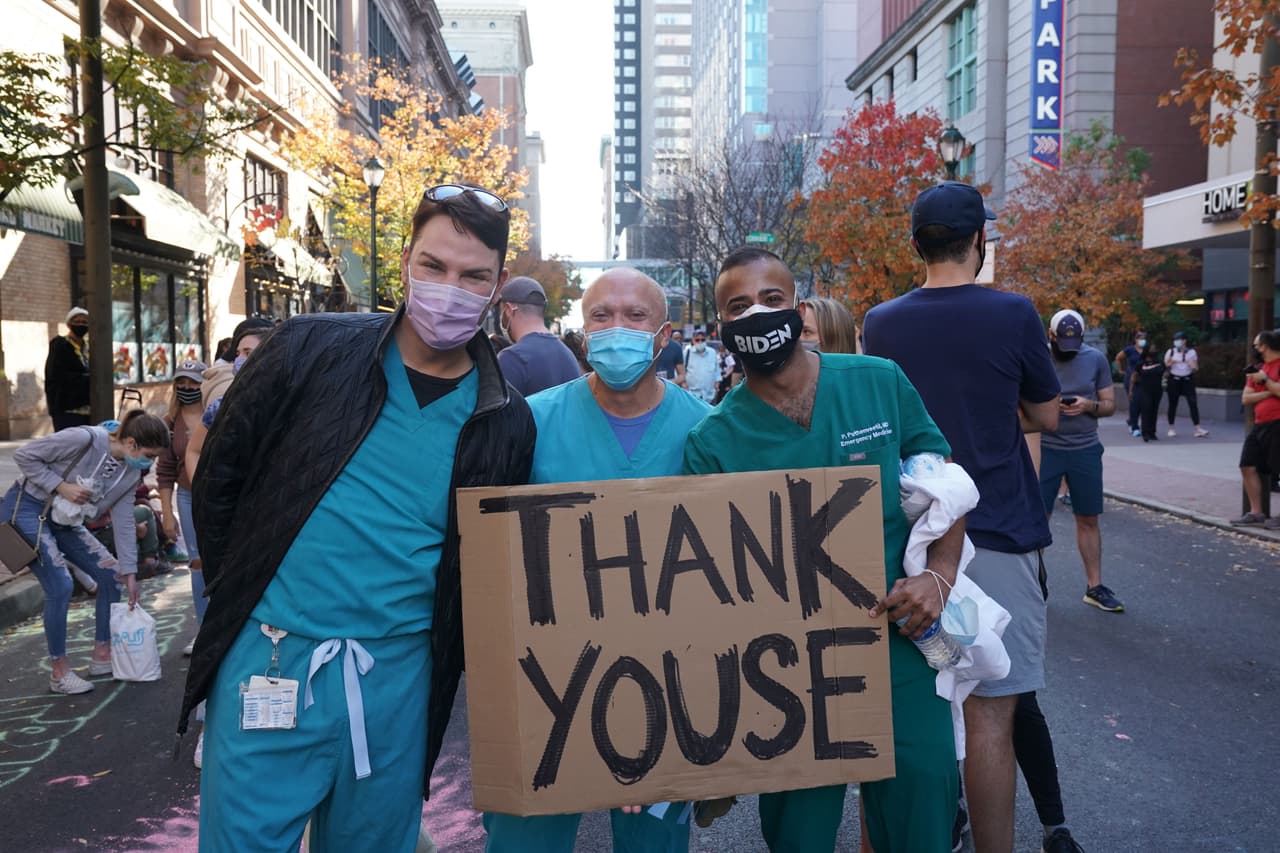 El personal médico del Hospital de la Universidad Thomas Jefferson sostiene un cartel mientras los partidarios de Biden celebran fuera del Centro de Convenciones de Pensilvania.