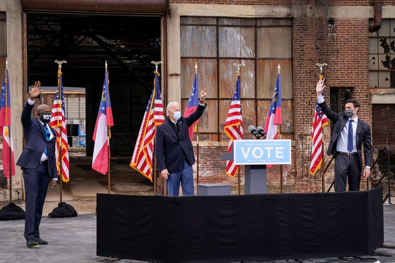 Al lado de los candidatos demócratas al Senado de Estados Unidos, el reverendo Raphael Warnock (izquierda) y Jon Ossoff (derecha), el presidente electo, Joe Biden, saluda a los asistentes a un evento de campaña desde los autos en Pullman Yard. La parada de Biden en Georgia se produce a menos de un mes de la segunda vuelta de las elecciones del 5 de enero, en la que buscan derrocar a los republicanos en funciones, el senador David Perdue y Kelly Loeffler.