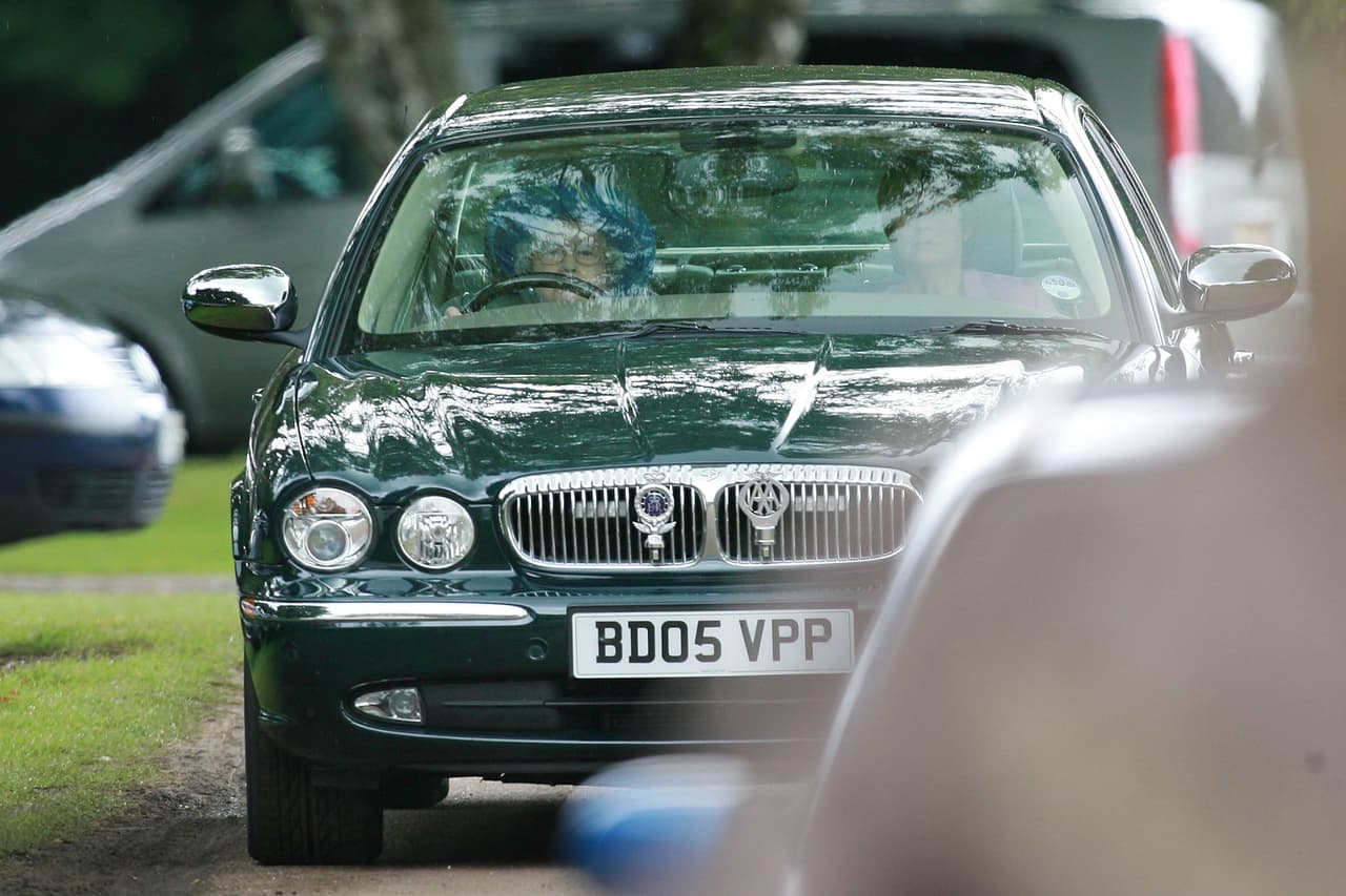 La reina isabel II tras el volante de una station wagon Jaguar X-Type. En la parrilla se pueden observar el emblema de la reina (derecha) y el de la Automobile Association.