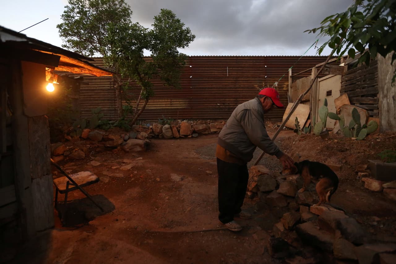 Pedro, el pensionado, acaricia a su perra 'Orejona'. Su patio: tierra árida, cactus, un enclenque árbol y... el muro de fondo.