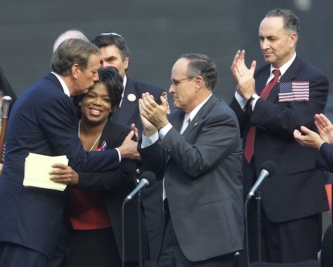 <b>Ovacionada por los políticos.</b> Oprah Winfrey acompañó a los líderes políticos y religiosos de la ciudad de Nueva York durante una oración pública por las víctimas de los ataques del 11 de septiembre de 2001, celebrado unos días después de la tragedia. Luego de dirigirse a la multitud que asistió al evento en el Yankee Stadium, Winfrey fue ovacionada por los presentes, entre ellos el senador demócrata Chuck Schummer y los republicanos George Pataki, gobernador del estado (quien la basa en la fotografía) y Ruddy Guliani, alcalde de la ciudad.