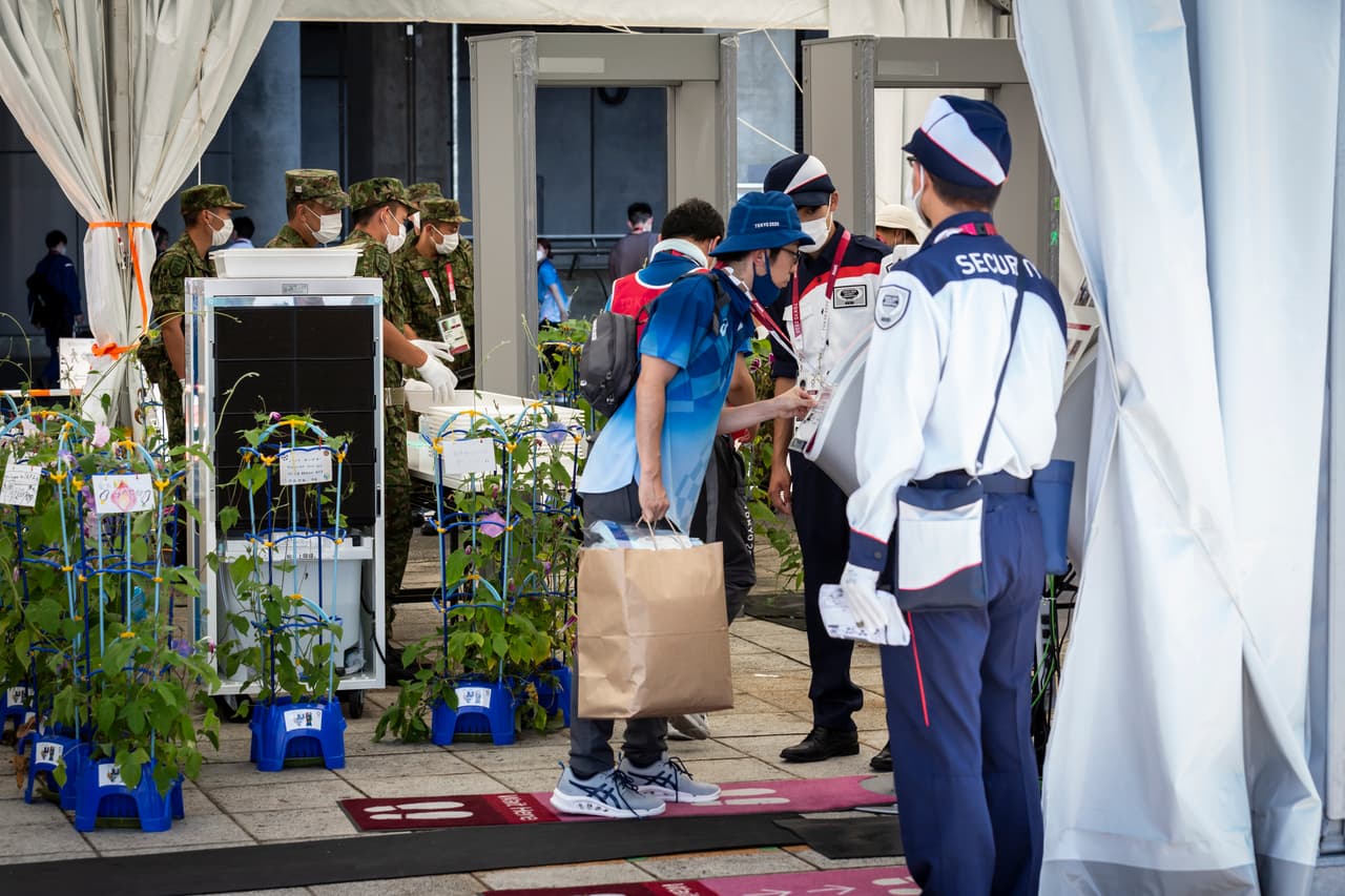 Varias figuras involucradas en la organización de los Juegos Olímpicos han sido despedidos antes de que comience oficialmente el evento. Entre ellos El director de la ceremonia de apertura de los Juegos Olímpicos, Kentaro Kobayashi, quien renunció la víspera del evento después de que 
<a href="https://www.univision.com/deportes/mas-deportes/organizador-tokio-2020-dimite-por-burlas-sobre-el-holocausto">aparecieran imágenes en las que parecía hacer bromas sobre el Holocausto</a>. 
<br>
<br>En la fotografía el punto de control de entrada al estadio internacional Yokohama el 22. Todas las personas se ven protegidas con mascarillas contra el covid-19.
<br>