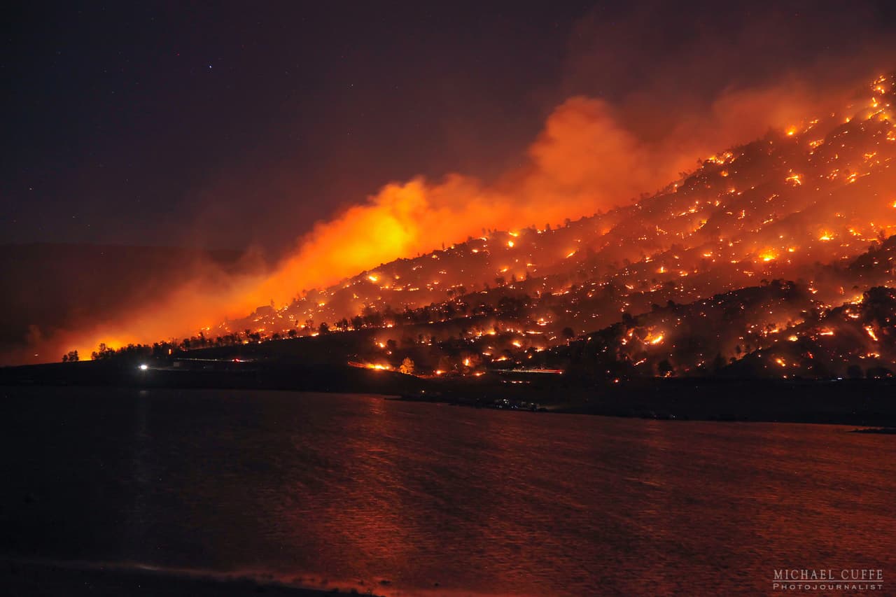 El fuego se precipita por la ladera y forma una columna humeante.
