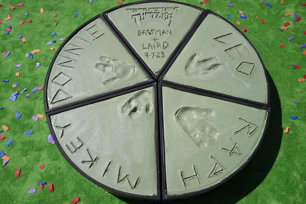 Junto a la firma de sus creadores, las huellas de las "manos" de Leonardo (Leo), Raphael (Raph), Michaelangelo (Mikey) y Donatello (Donnie), completan una pizza, su alimento preferido.