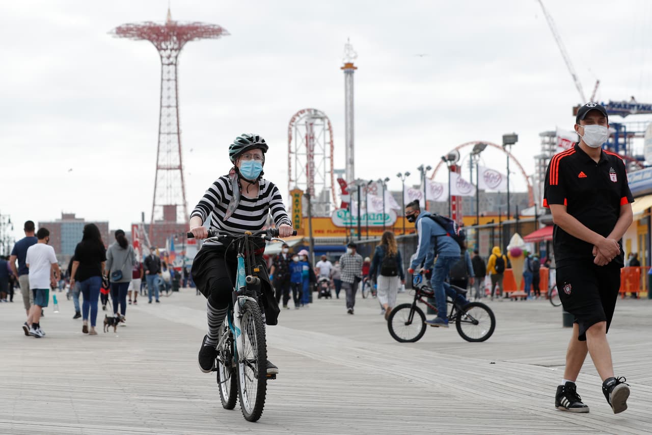 Una mujer con mascarilla monta su bicicleta este domingo 24 de mayo del 2020 en el paseo marítimo de Coney Island, en Nueva York, el fin de semana de Memorial Day, que marca el tradicional comienzo del verano en el país.