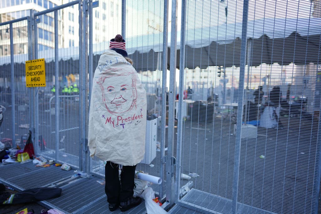 Un
<b>simpatizante con una frazada con el rostro de Trump</b> mira a través de una reja en medio de una calle llena de basura.