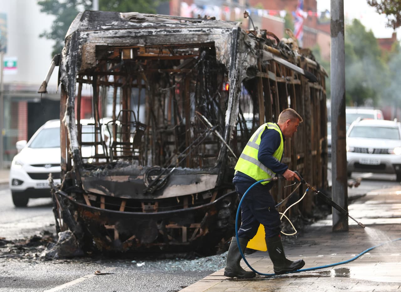 Un trabajador retira los escombros frente a un autobús calcinado tras los disturbios ocurridos en Belfast, Irlanda del Norte. (Foto AP/Peter Morrison)