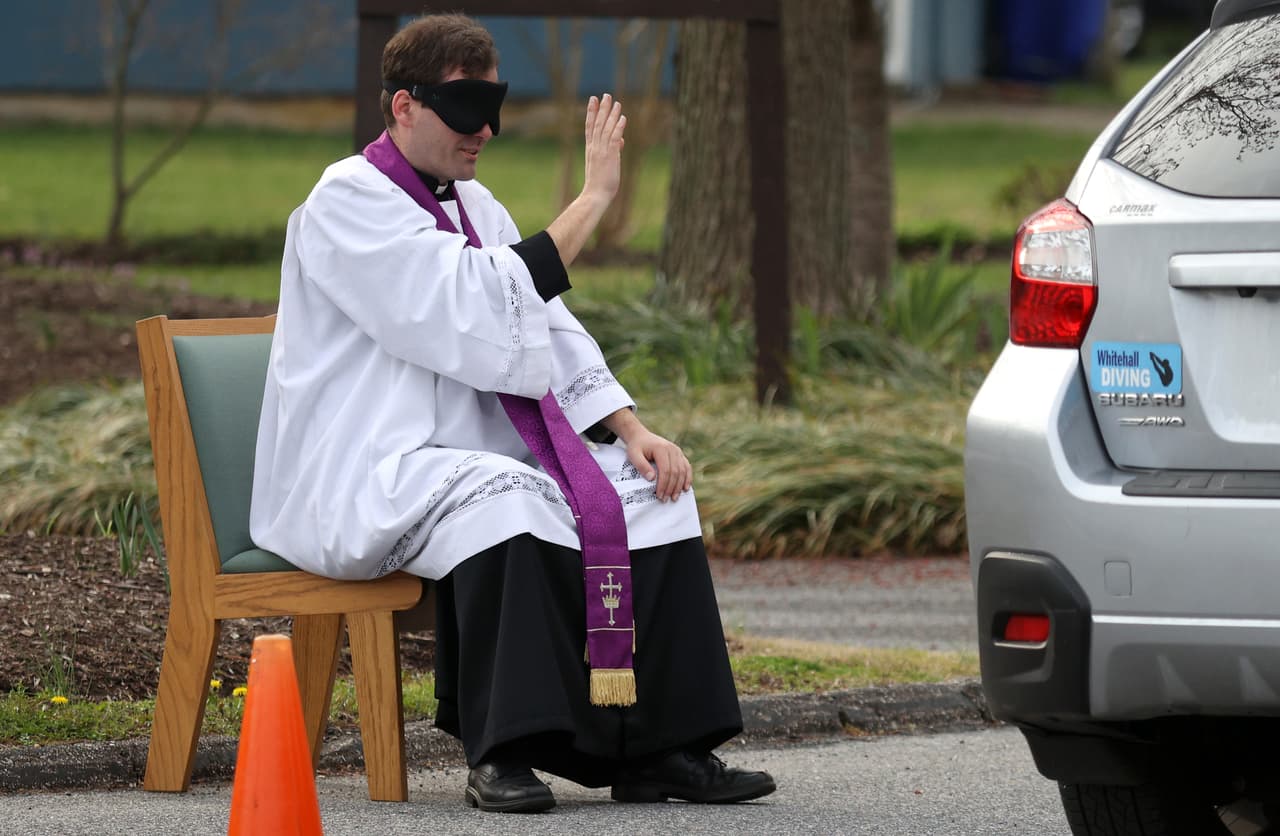 <b>Un confesionario de servicio en el auto.</b> El Padre Scott Holmer, de la Iglesia Católica San Eduardo,en Bowie, Maryland, realiza confesiones a una fila feligreses en el estacionamiento del templo, el 20 de marzo. En EEUU al menos 70 millones de personas permanecen en casa y en decenas de comunidades solo están disponibles los servicios esenciales, para evitar que se propague el contagio del coronavirus.