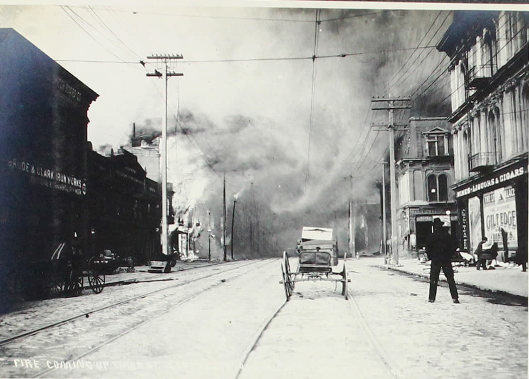 Un hombre observa junto a un vehículo cómo el humo avanza por una avenida.